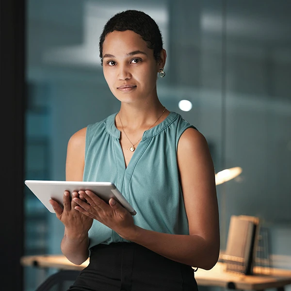 Professional woman holding a tablet in a modern office, looking towards the camera