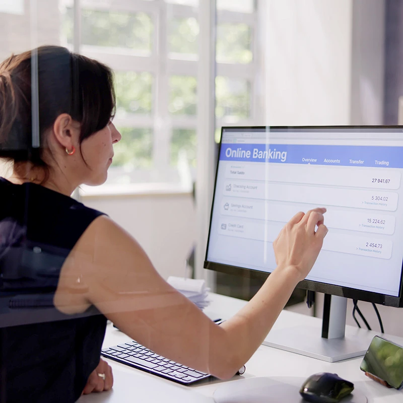 Woman tapping an online banking dashboard on a desktop computer in a bright office