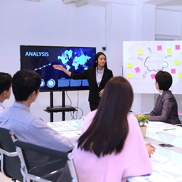 Presenter pointing to an analysis dashboard on a screen while colleagues in a meeting room look on