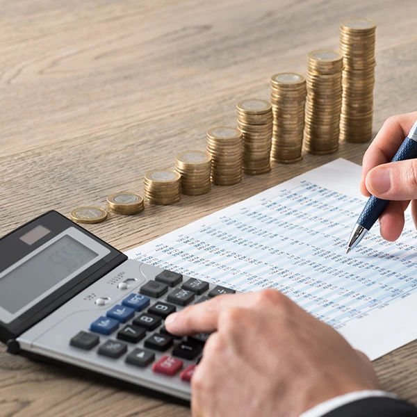 Person using a calculator and reviewing financial data on paper, with neatly stacked coins in the background symbolising profit growth and financial planning.
