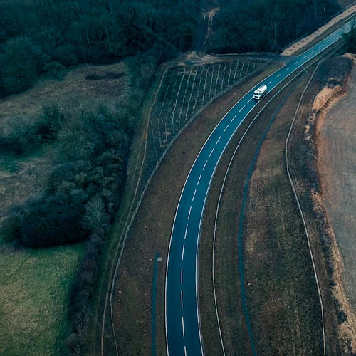 Aerial view of a winding countryside road surrounded by fields and trees, with a single vehicle travelling along it. The image conveys motion, direction, and progress, symbolising strategic journeying, business growth, or forward planning