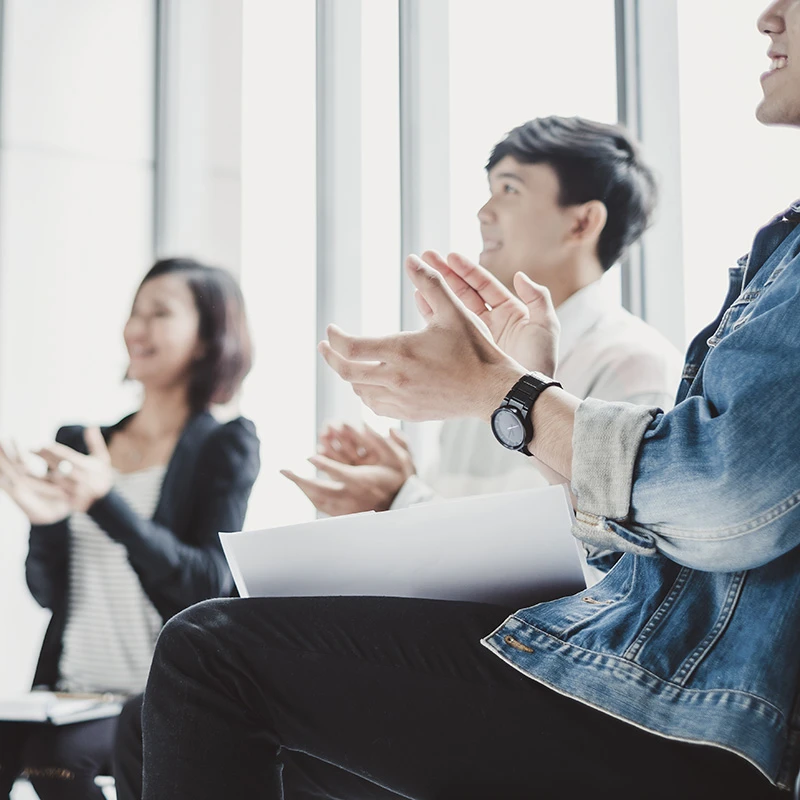 Group of people sitting and clapping during a meeting or presentation, showing appreciation or engagement.