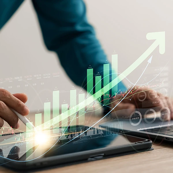 Person using a stylus and laptop to analyse financial performance data, with a digital overlay of green bar and line graphs showing upward growth trends, representing investment analysis and business performance improvement.