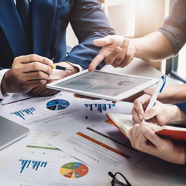 Close-up of business professionals reviewing charts and graphs on paper and a tablet during a marketing strategy meeting
